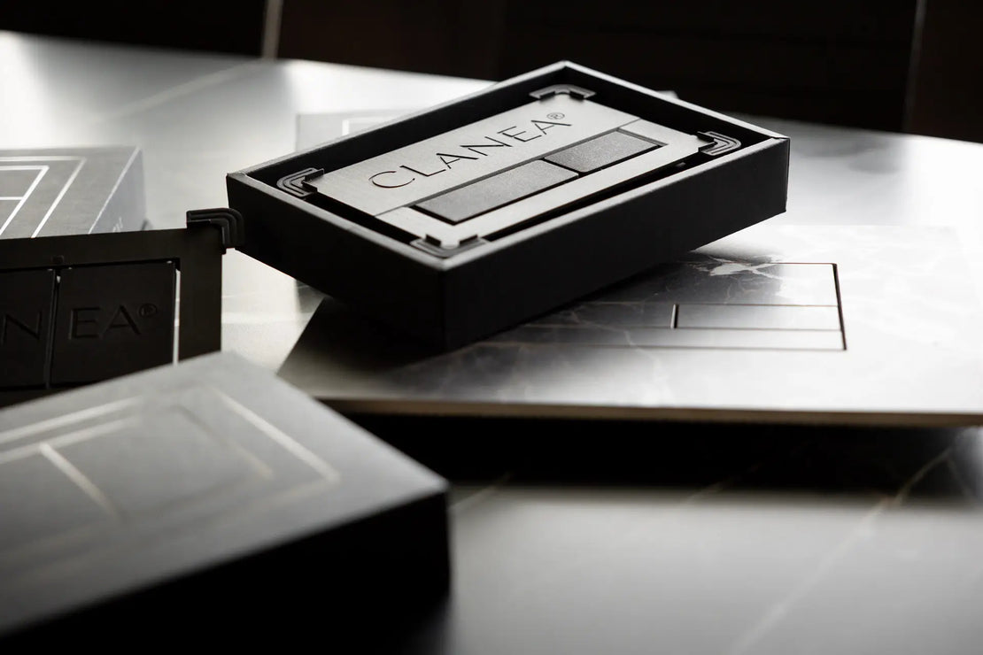 Clanea PurePlate – hochwertige WC-Betätigungsplatte in schwarzem Design, Swiss Made, präsentiert in edler Verpackung auf Marmoroberfläche.